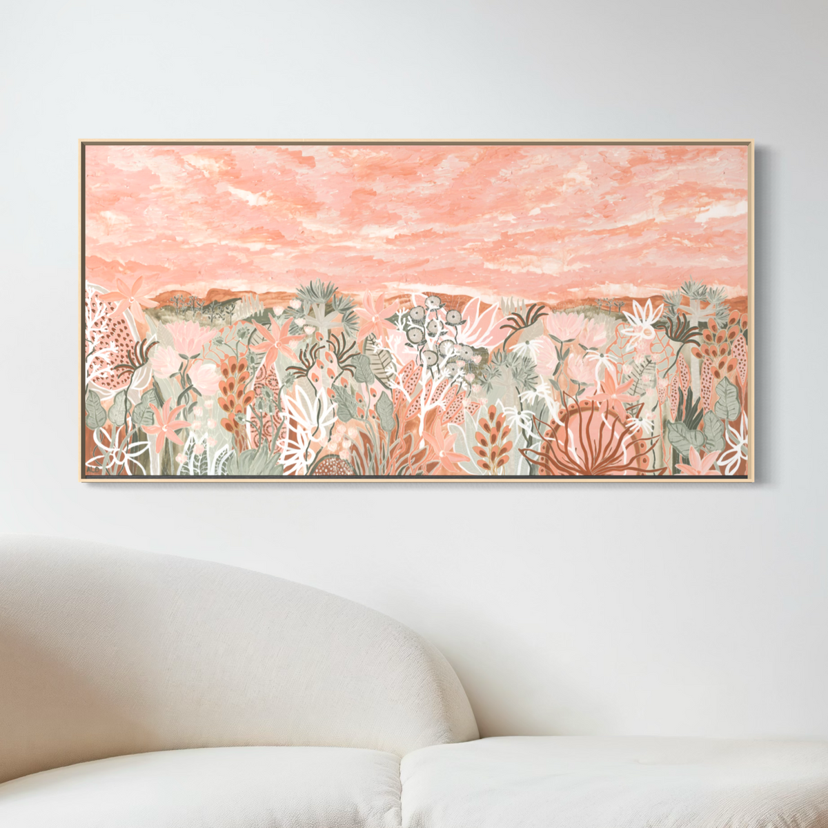 Valley of the Fairy Floss Flowers by Anna Lohe – framed extra-wide artwork with a blush pink sky over peach and sage native flora, above a white sofa