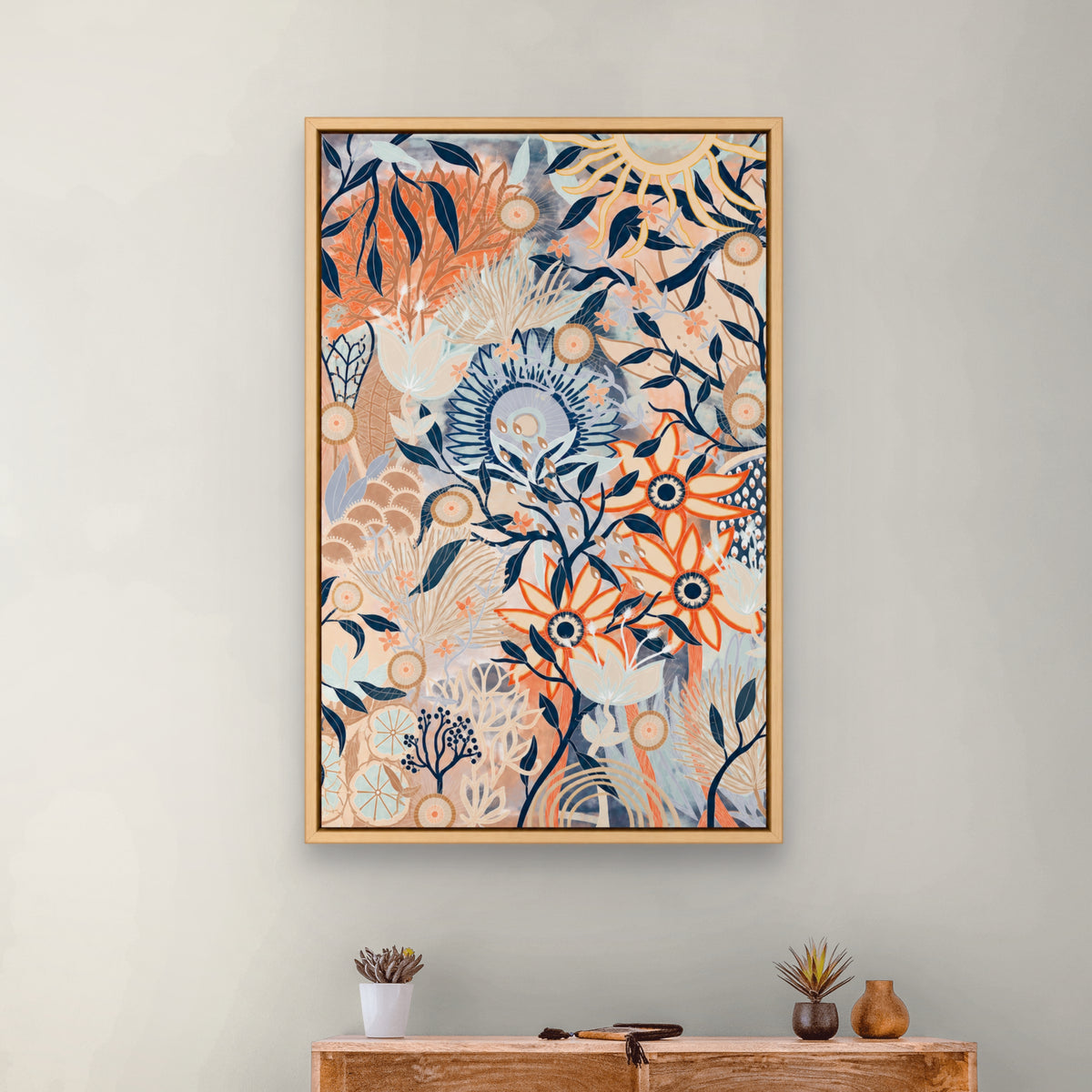 A framed botanical art print with orange, blue, and beige floral motifs hangs on a light gray wall above a wooden console table with small decorative plants.