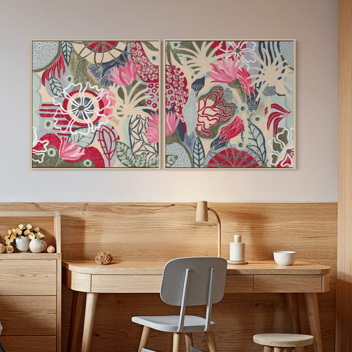 Two framed botanical art prints with pink, red, blue, and beige floral patterns hang on a beige wall above a light wood desk and chair in a modern room.
